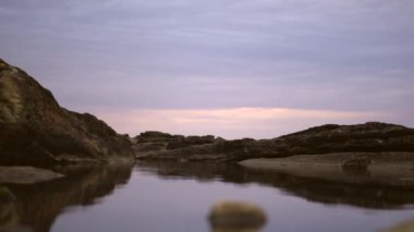 Güzel siyah bir elbise içinde gezinen genç bir kadın. Yazın gün batımında deniz kenarında kayalıklarda şeffaf uzun siyah elbiseli esmer bir kadının yaşam tarzı..