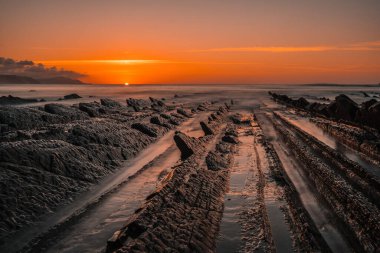The incredible Flysch, a beautiful sunset in Sakoneta, is a beach in Deba. It is the western end of the Geopark of the Basque Coast, Guipuzkoa, Basque Country. The sun goes down clipart