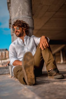 Beyaz gömlekli, güneş gözlüklü, gülümseyen bir adam.