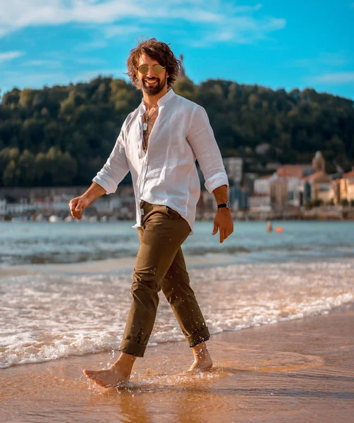 portrait of barefoot man in white shirt walking on sandy beach