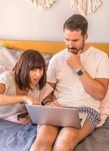 A Caucasian couple on the bed with a computer and a phone, making a reservation at a hotel or flight, organizing vacations, new technologies in family. Looking at the best deals