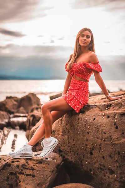 在基普兹科亚的祖迈亚市 一名身穿红色连衣裙的年轻的黑发白人妇女在伊兹鲁恩海滩上 巴斯克乡村 在日落时 生活方式的一部分 在海边的岩石上 — 图库照片