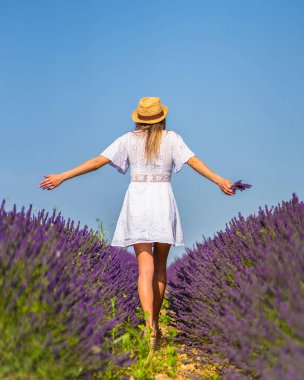 Kırsal yaşam tarzı, beyaz elbiseli ve lavanta tarlasında mor çiçeğiyle saman şapkalı beyaz bir kadın. Navarra, İspanya. Açık kollarla yürüyorum