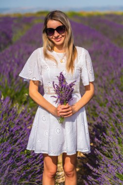 Kırsal yaşam tarzı, beyaz elbiseli beyaz sarışın kadın ve Olite 'deki mor çiçeğiyle lavanta tarlasında güneş gözlüğü. Navarra, İspanya. Güzel kırsalda portre