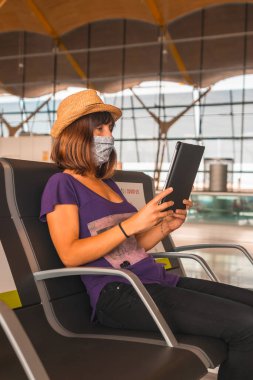 Koronavirüs salgınında hava yolculuğu, güvenli seyahat, sosyal mesafe, yeni normal. Yüzü maskeli genç bir kadın kalkmayı bekliyor, havaalanları neredeyse boş.