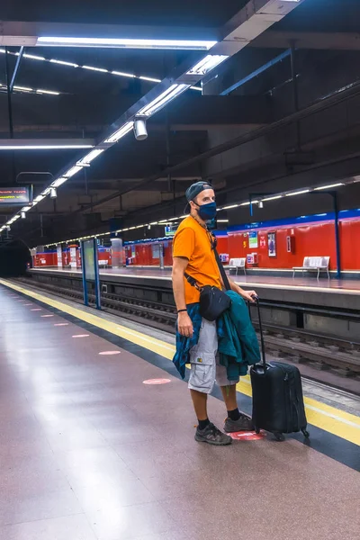 Tourist travel by metro in the coronavirus pandemic, safe travel, social distance, a new normal. A young man with a suitcase waiting for the subway