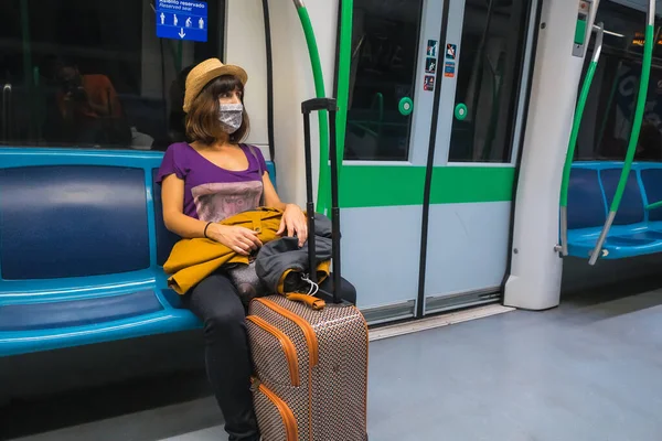 Tourist travel by metro in the coronavirus pandemic, safe travel, social distance, a new normal. A young girl with a face mask traveling sitting inside the subway with a suitcase