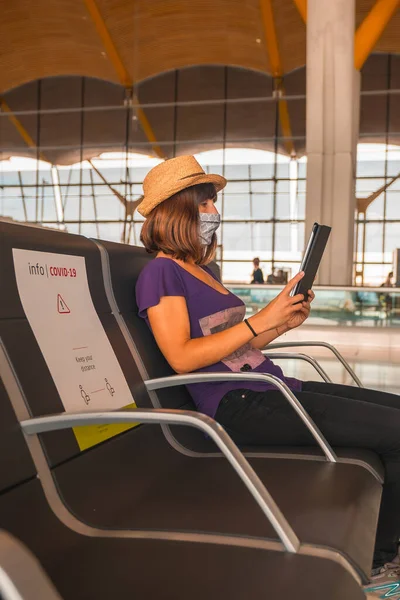 Air travel in the coronavirus pandemic, safe travel, social distance, new normal. A young woman with a face mask sitting waiting to take off, airports almost empty