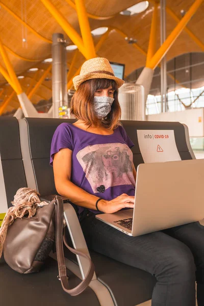 Air travel in the coronavirus pandemic, safe travel, social distance, new normal. A young woman with a face mask working with a computer waiting to take off, almost empty airports