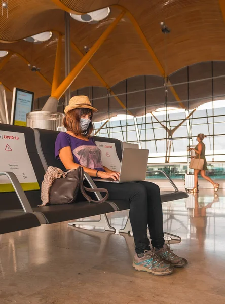 Air travel in the coronavirus pandemic, safe travel, social distance, new normal. A young woman with a face mask working with a computer waiting to take off, almost empty airports
