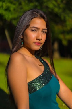 Dar yeşil bir elbise giyen, uzun düz saçlı, güzel, esmer bir Latin. Yazın parkta genç bir kadının portresi.