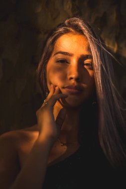 Yüzünde hafif bir ışıkla bir ağaca yaslanmış genç bir Latin esmer. Gülümseyen bir portre