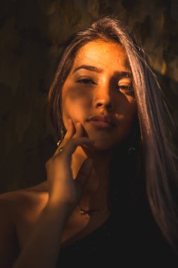 Yüzünde hafif bir ışıkla bir ağaca yaslanmış genç bir Latin esmer. Ciddi yüzlü bir portre.