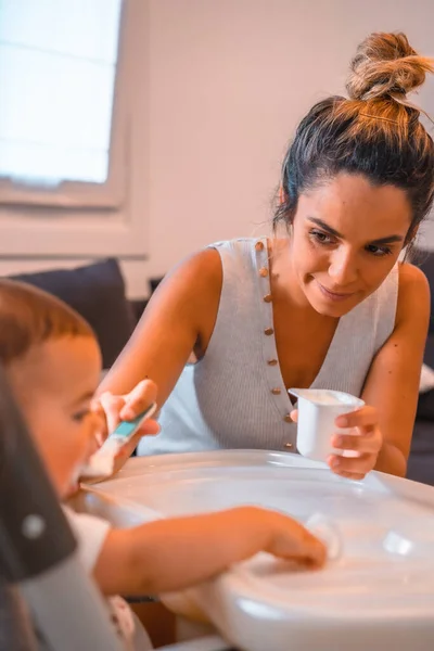 Young Caucasian Mother Feeding Her Son Yogurt While Sitting Highchair — Stock Photo, Image
