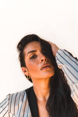 Yaşam tarzı, düz saçlı, beyaz takım elbiseli, siyah çizgili esmer kız. Beyaz bir arka planda. Kameraya farklı pozlarda bakan genç bayana portre