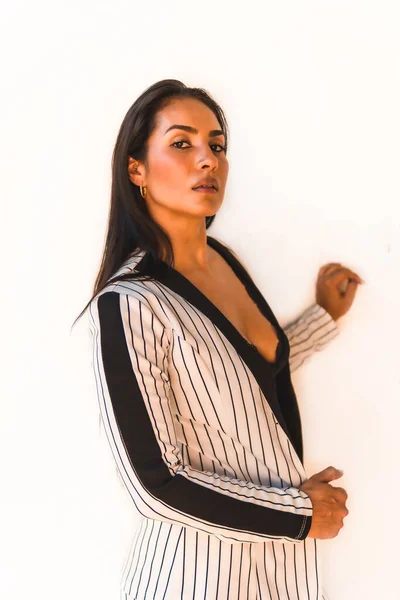 Lifestyle, straight-haired Latin brunette girl in a white suit and black stripes. On a white background. Looking at the camera, in different postures, fashion editorial