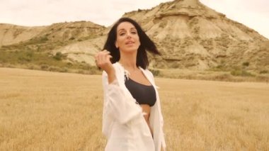 Yazın Bardenas Reales 'te beyaz kimonolu esmer bir manken ve siyah bir bikini pozu vermek. Yaşam tarzı, Navarra, İspanya. 4k video