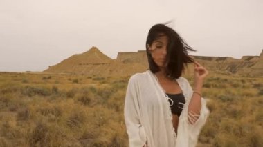 Yazın Bardenas Reales 'te beyaz kimonolu esmer bir manken ve siyah bir bikini pozu vermek. Yaşam tarzı, Navarra, İspanya. 4k video