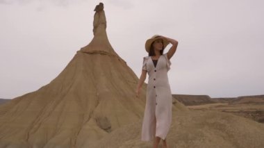 Beyaz elbiseli ve şapkalı beyaz tenli genç beyaz tenli Bardenas Reales 'teki Castildetierra' da yürüyor. Yaşam tarzı, Navarra, İspanya. 4k video