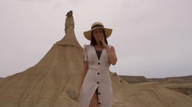 Beyaz elbiseli ve şapkalı beyaz tenli genç beyaz tenli Bardenas Reales 'teki Castildetierra' da yürüyor. Yaşam tarzı, Navarra, İspanya. 4k video