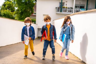 Yüz maskeli üç kardeş okula dönmeye hazır. Yeni normallik, sosyal mesafe, koronavirüs salgını, covid-19. Tüm güvenlik önlemleriyle birlikte evi terk ediyor.