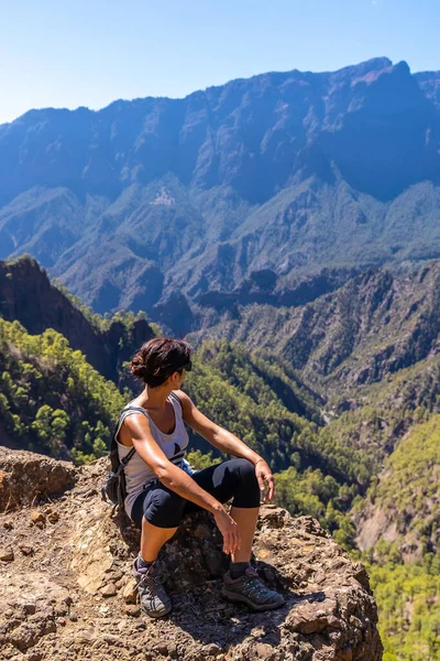 A young woman resting after trekking on top of La Cumbrecita sitting in the natural viewpoint looking at the mountains of the Caldera de Taburiente, La Palma island, Canary Islands, Spain