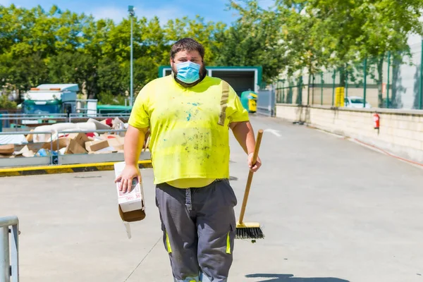 Worker in a recycling factory or clean point and garbage with a face mask and with security protections, new normal, coronavirus pandemic, covid-19. Operator cleaning and ordering the installation