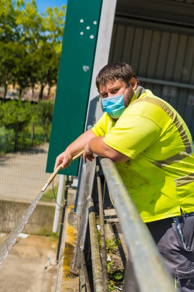 Worker in a recycling factory or clean point and garbage with a face mask and with security protections, new normal, coronavirus pandemic, covid-19. Portrait of worker cleaning with hose