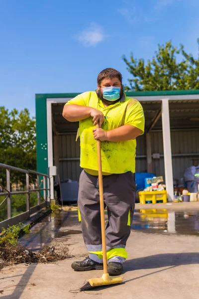 Worker in a recycling factory or clean point and garbage with a face mask and with security protections, new normal, coronavirus pandemic, covid-19. Portrait worker with a broom