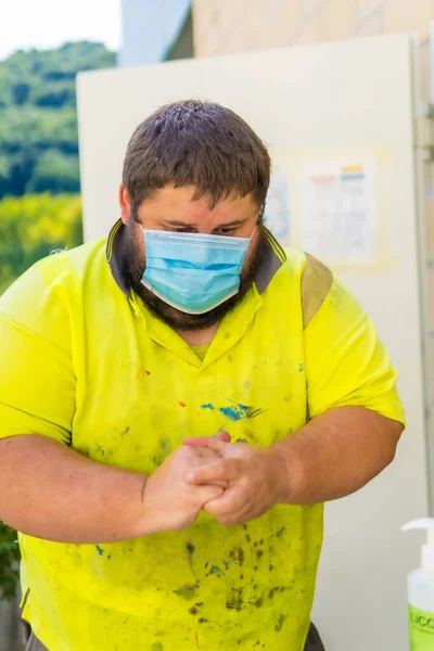 Worker in a recycling factory or clean point and garbage with a face mask and plastic protective screen, new normal, coronavirus pandemic, covid-19. Cleaning your hands with disinfectant liquid