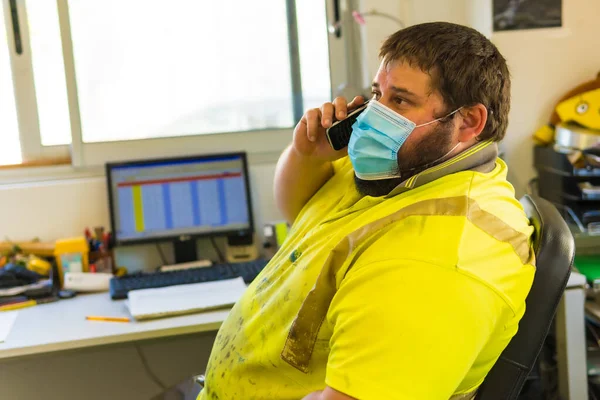 Worker in a recycling factory or clean point and garbage with a face mask and plastic protective screen, new normal, coronavirus pandemic, covid-19. Talking on the phone in the office