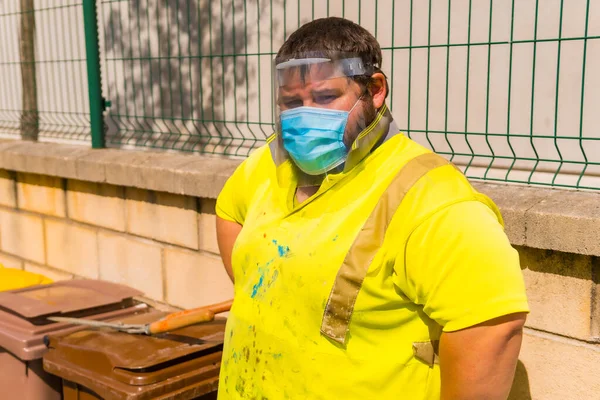 Worker in a recycling factory or clean point and garbage with a face mask and plastic protective screen, new normal, coronavirus pandemic, covid-19. Plant worker portrait
