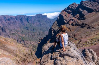 A young woman sits resting and looking at the views of the Roque de los Muchachos national park on top of the Caldera de Taburiente, La Palma, Canary Islands. Spain clipart