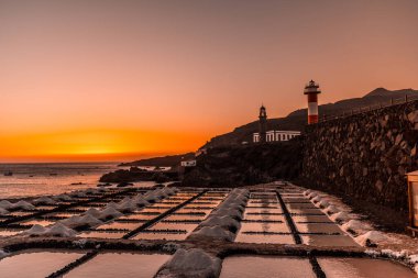 Tuz düzlüklerinde turuncu gün batımı ve arka planda Fuencaliente Deniz feneri La Palma adasının güneyindeki volkanların rotasında, İspanya 'nın Kanarya Adaları' nda.