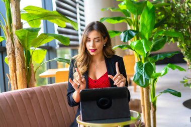 Genç sarışın, beyaz girişimci bir video konferansı düzenliyor siyah ceket ve kırmızı elbise, telekomünikasyon, yeni normal, pembe bir kanepede oturuyor.