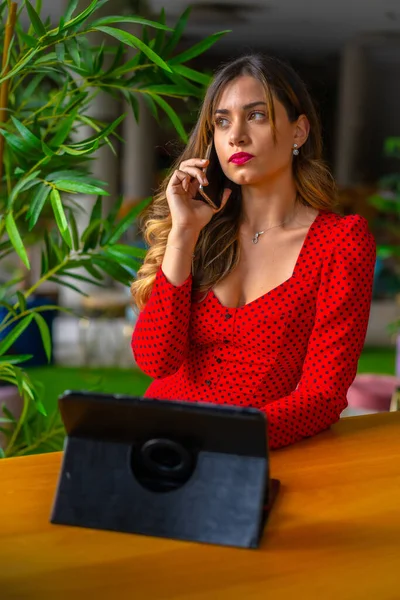 Sarışın, beyaz bir girişimci bir şehir otelinden iş videosu çekiyor. Tablet, kırmızı yönetici elbisesi, telekomünikasyon, otellerde çalışıyor.