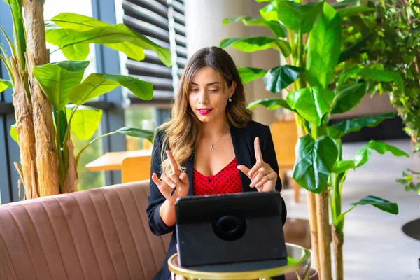 Genç sarışın, beyaz girişimci bir video konferansı düzenliyor siyah ceket ve kırmızı elbise, telekomünikasyon, yeni normal, pembe bir kanepede oturuyor.