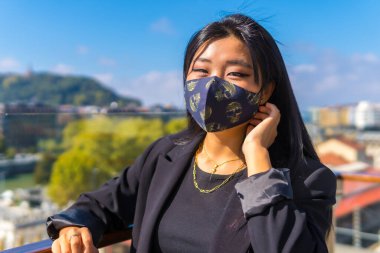 Genç Çinli esmer turist, maskesini takıp yeni normal tatilinde şehre geliyor. Asyalı kız yaz yaşam tarzı, sosyal uzaklık, covid-19, coronavirüs