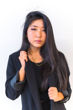 Siyah ceketli genç Asyalı kız beyaz arka planlı kameraya bakıyor. Çin uyruklu genç bir kızın yaşam tarzı.