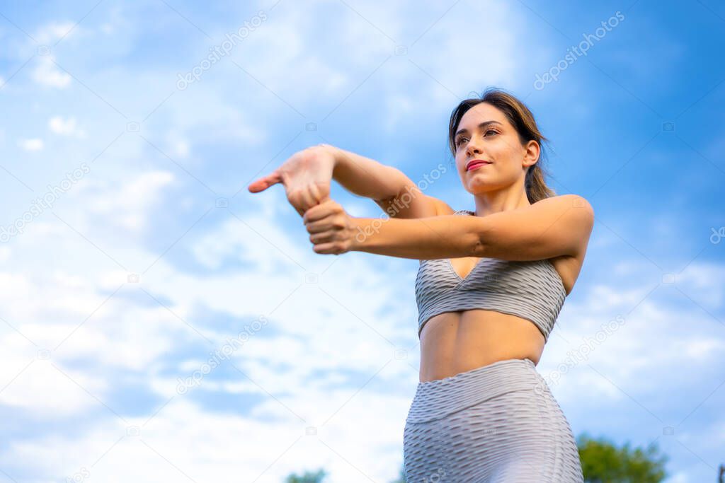 Fitness session with a young Caucasian blonde, very cheerful doing stretching, with the sky in the background, exercising in the field, gray sport suit, fit girl, healthy life