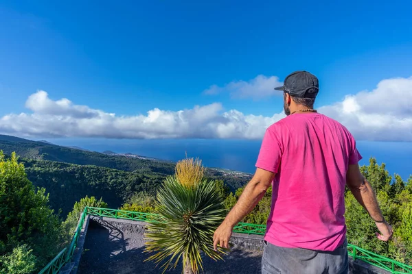A young man in a pink t-shirt on top of the mountain at the viewpoint of the Cubo de la Galga natural park on the northeast coast on the island of La Palma, Canary Islands. Spain