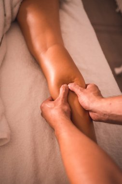 Masada yatan genç bir bayanın sağ bacağının arkasında bir fizyoterapistin masajının detayları. Fizyoterapi, osteopati, rahatlatıcı masaj, sırtında tedavi videosu.