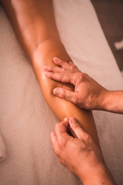 Masada yatan genç bir bayanın sağ bacağının arkasında bir fizyoterapistin masajının detayları. Fizyoterapi, osteopati, rahatlatıcı masaj, sırtında tedavi videosu.
