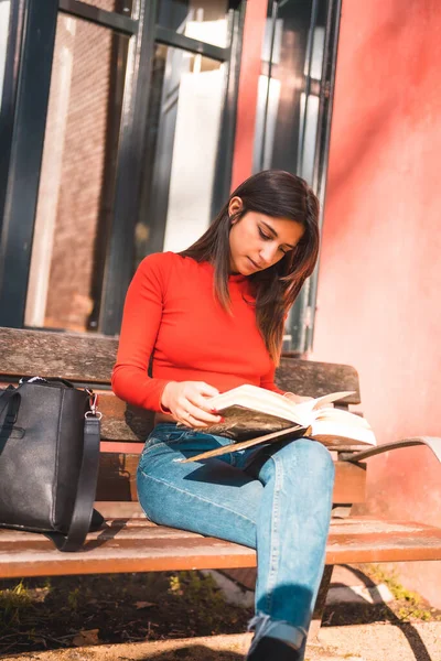 ライフスタイル 公園のベンチに座って本を読んでいる赤いシャツの若い白人のブルネット 垂直写真 — ストック写真