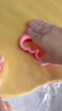 Taze hamur üzerinde çeşitli şekillerde pembe kurabiye keskisi kullanan küçük eller Noel kurabiyeleri yaratıyor.
