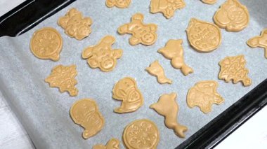 Ev yapımı şenlikli Noel kurabiyeleri parşömen tepsisinde altın kahverengiler pişiriyor, ren geyiği, kardan adam ve ağaç şekilli tatil şekilleri sunuyor.