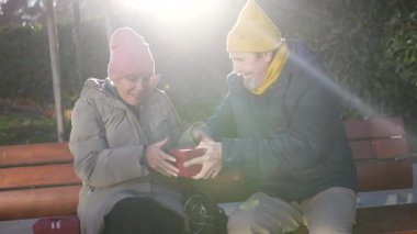 Yaşlı bir çift, parkta bir bankta Noel hediyelerini değiş tokuş ederken sevgi ve şefkat dolu bir anı paylaşıyorlar.