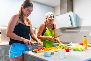 İki kadın birlikte yemek pişirmekten zevk alıyor. Parlak, modern bir mutfakta taze sebzeler hazırlıyorlar. Aile bağlarını ve aşçılık becerilerini sergiliyorlar.