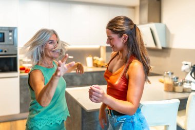 Mutlu anne ve kız modern mutfaklarında birlikte dans ediyorlar, aile bağlarının kaygısız anının tadını çıkarıyorlar.