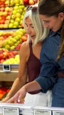 Anne ve kız süpermarkette taze ürünleri gösterip tartışıyorlar, sağlıklı yiyecek seçimleri yapıyorlar.